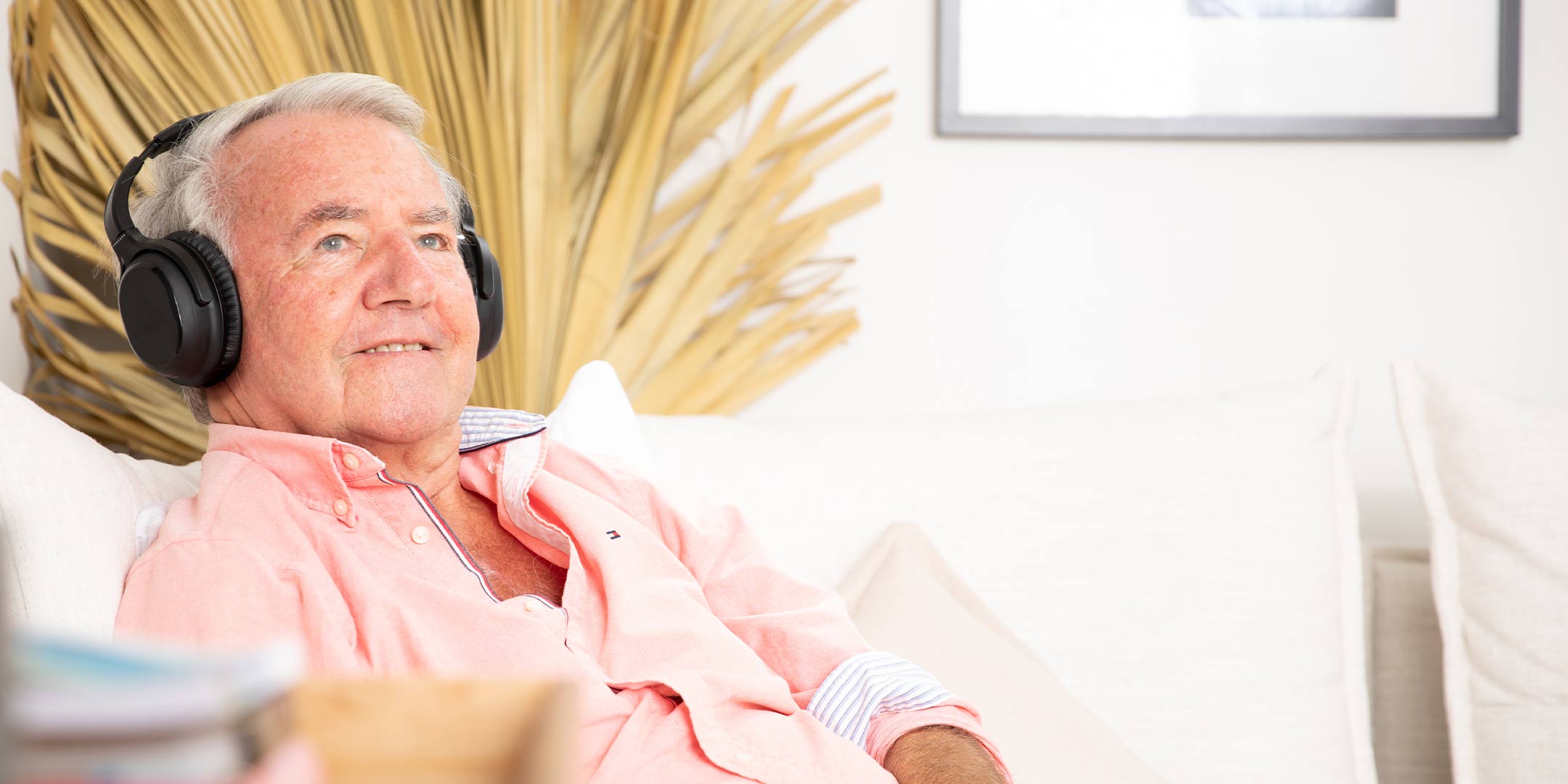 A man smiling contently sitting on the couch while listening to music on his Audeara headphones