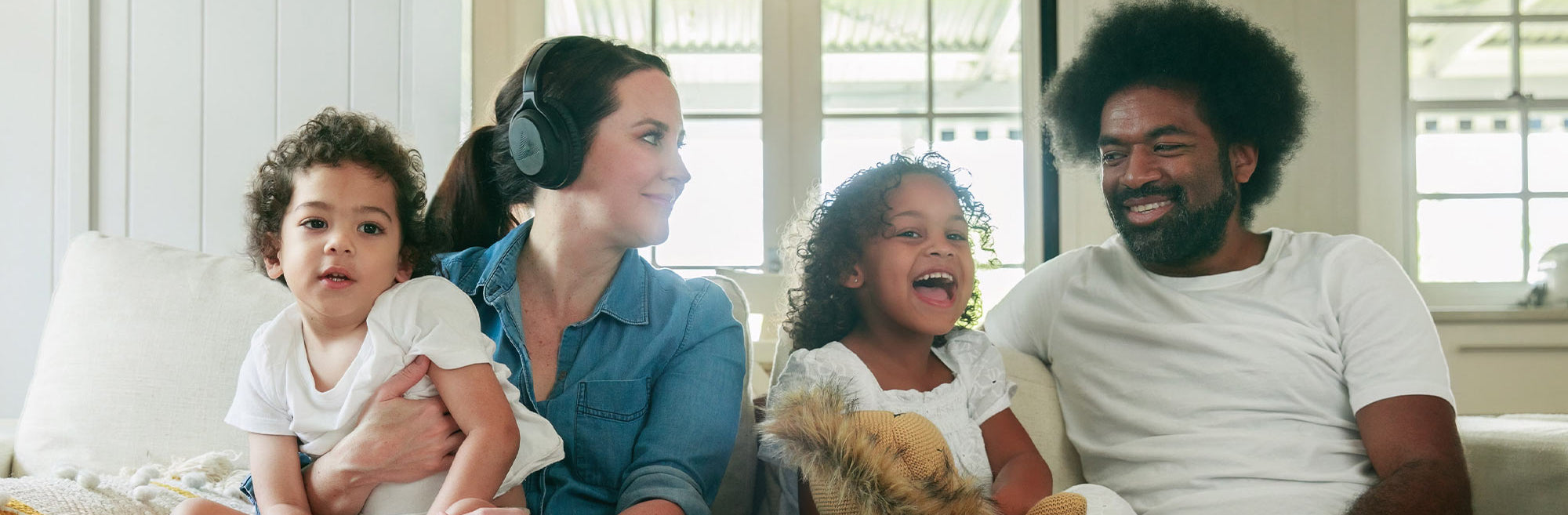 Family on a couch watching TV together, with the Mum wearing Audeara headphones.