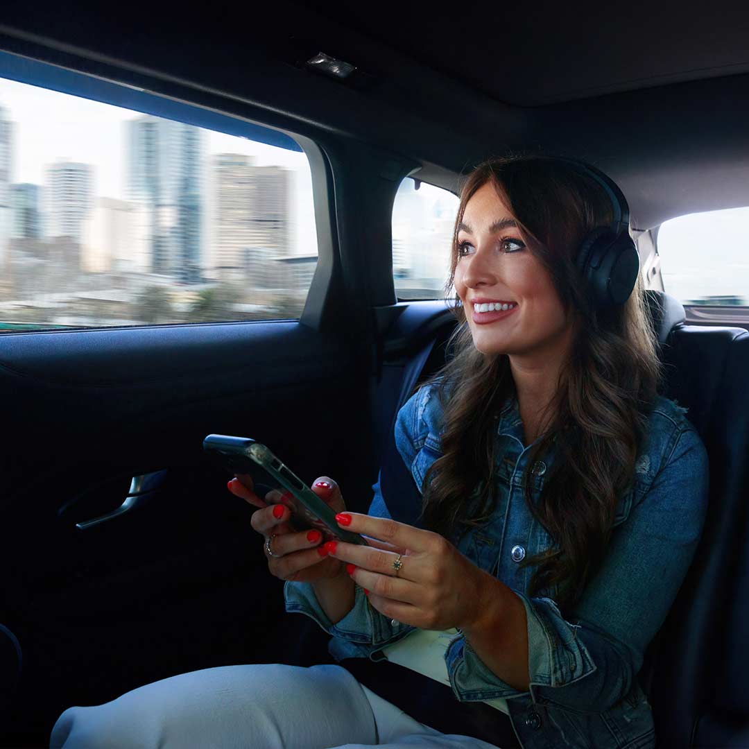 Woman wearing Audeara headphones in the back seat of a car with the world outside blurred from speed through the window