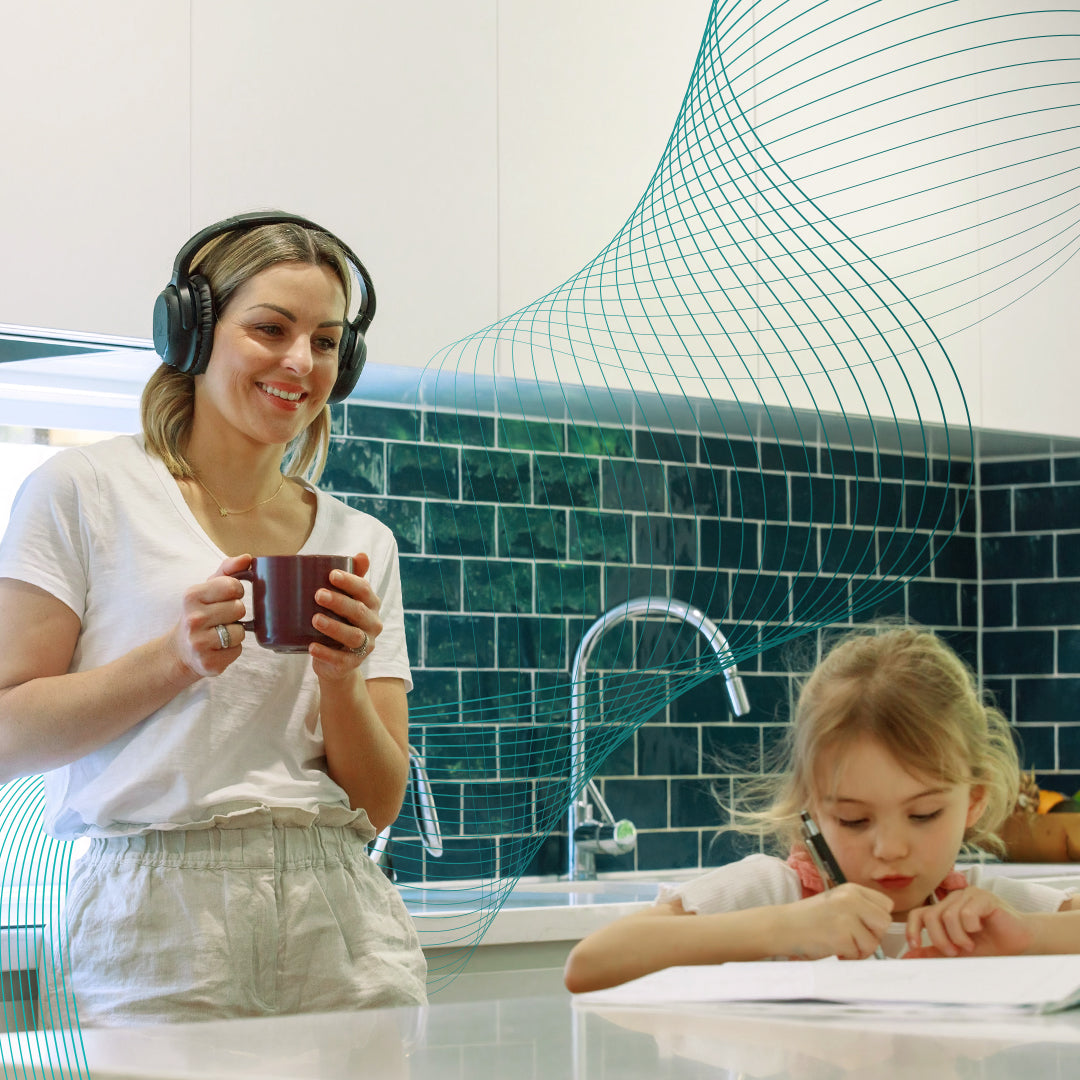 A mum wearing Audeara headphones in her kitchen at home watching her child draw at the counter