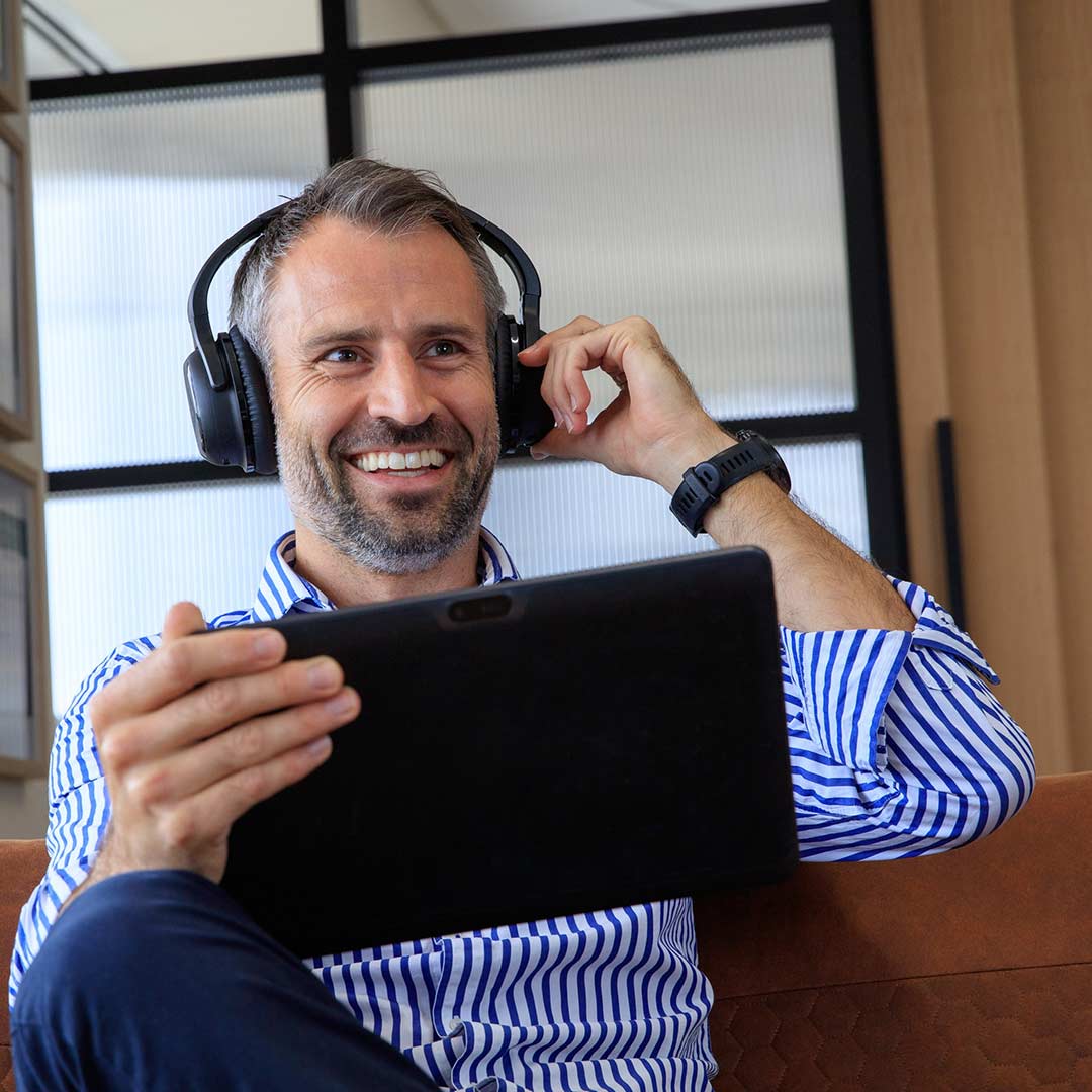 Man smiling and wearing Audeara headphones and holding a tablet in an office