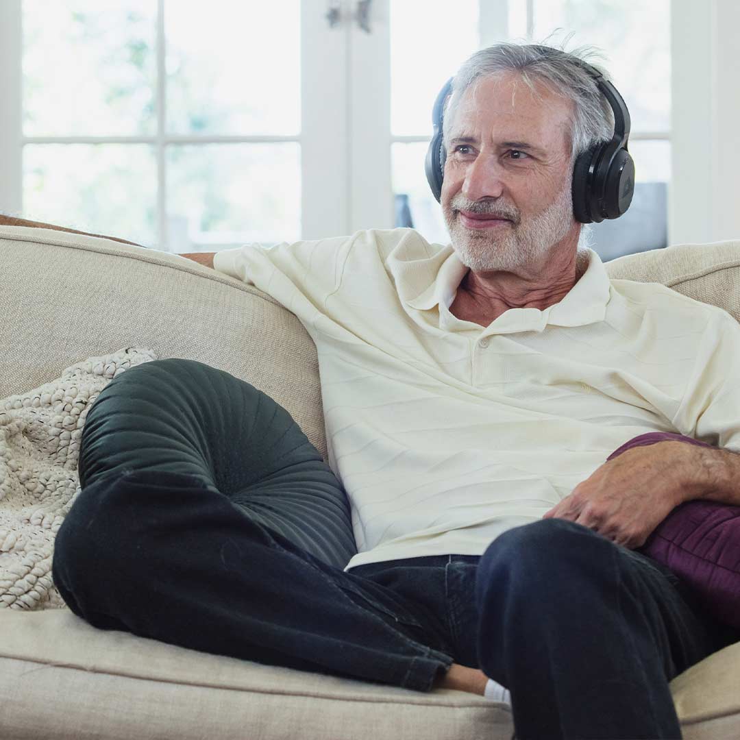 Man on couch wearing Audeara headphones watching TV