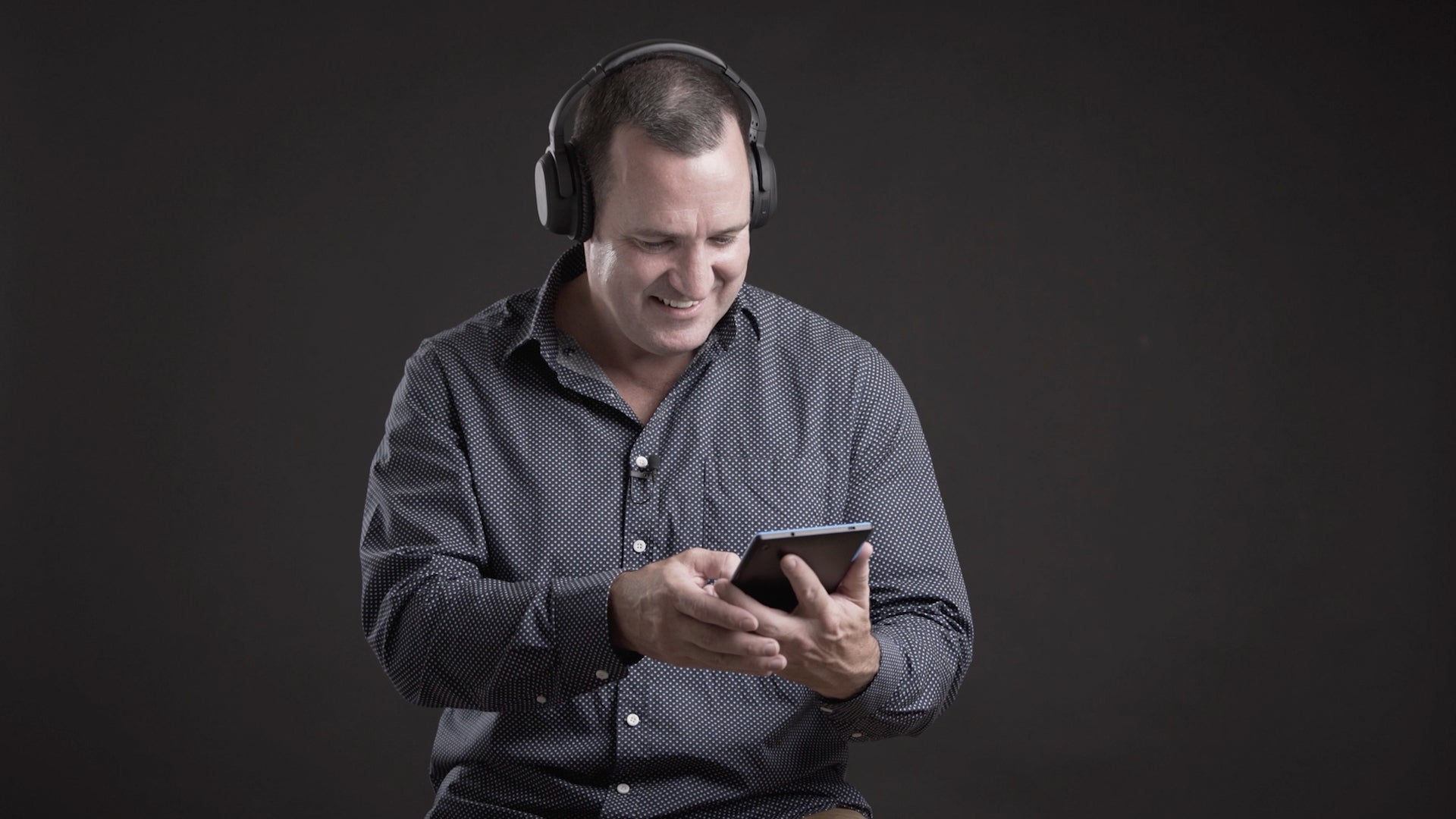 A man wearing Audeara headphones, smiling and looking down at a phone doing the hearing health check using the Audeara app